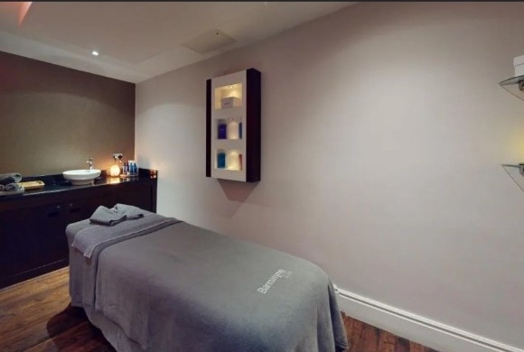 Softly lit single treatment room at Bannatyne Spa Luton, with a treatment bed, folded towels and a basin